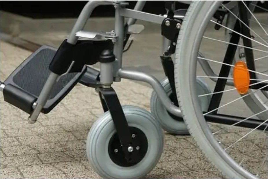 Close-up of a manual wheelchair wheel, footplate and castor on a paved path