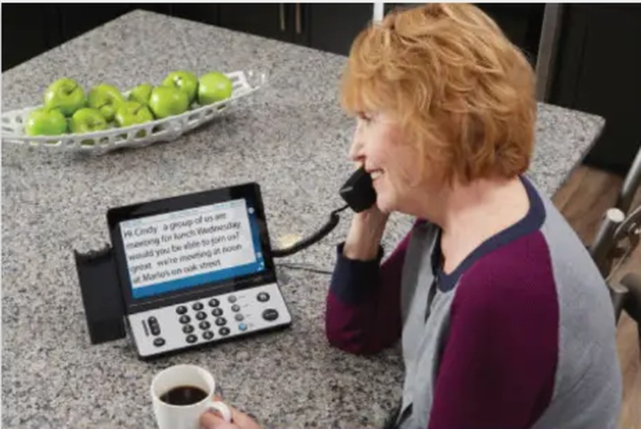 A woman at her kitchen counter using a captioned telephone