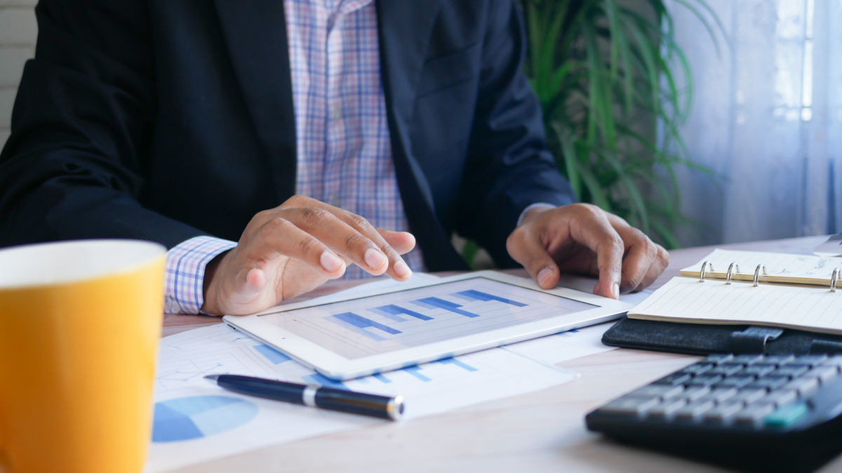 A person at a desk reviewing charts on a tablet beside a calculator and planner